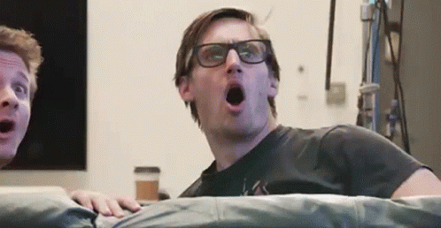 Man With Glasses on Couch Mouth Open Another Man Watching