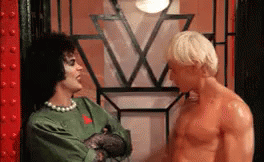 Man With Long Blonde Hair And Bald Head Standing Shirtless In Dark Room GIF