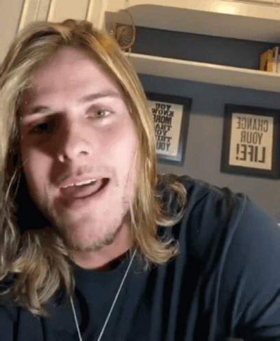Man With Long Blonde Hair Smiling in Front of Change Sign