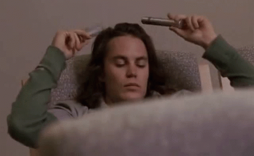 Man With Long Hair Laying in Chair Holding Pipe to Head