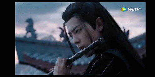 Man with Long Hair Playing Flute in Dark Room