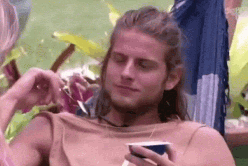 Man With Long Hair Sitting in Hammock Holding Coffee