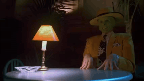 Man With Mask Sitting At Table With Lamp GIF