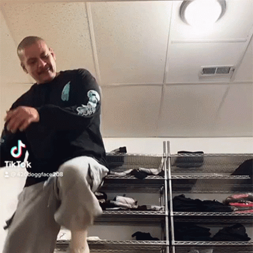 Man With Mustache Dancing In Front Of Clothes Rack With TikTok Logo GIF