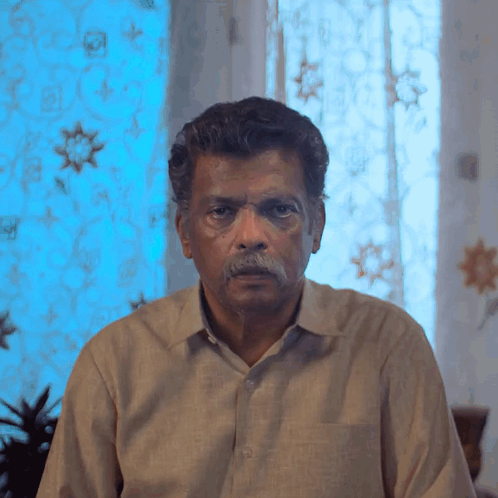 Man With Mustache Looking at Camera in Front of Blue Curtain