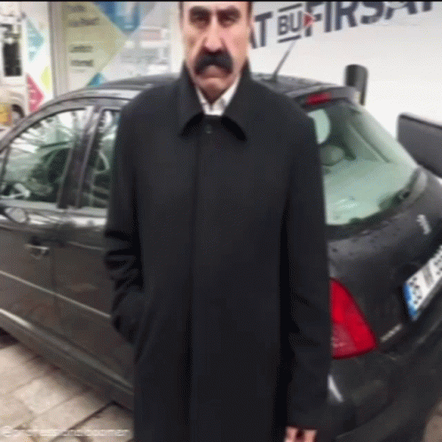 Man With Mustache Standing in Front of Car Saying It Bu Firsa