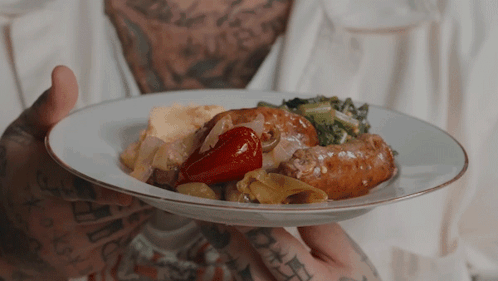 Man With Tattoos Holding Plate of Food With Sausage and Vegetables