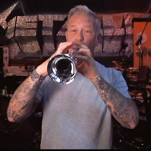Man With Tattoos Playing Trumpet In Dark Room GIF
