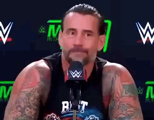 Man With Tattoos Talking Into Microphone Wearing But Shirt