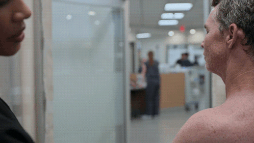 Man Without Shirt Talking to Woman in Hospital Hallway