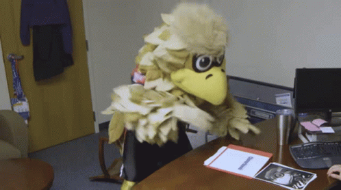 Mascot in Bird Costume Sitting at Desk