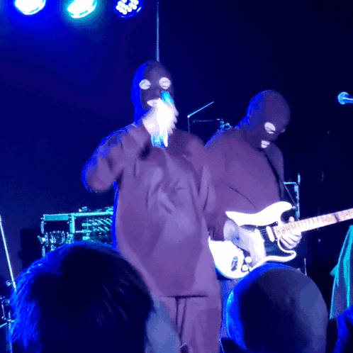 Masked Man Singing Into Microphone Playing Guitar
