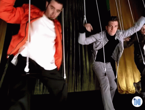 Men Dancing In Front Of Yellow Curtain With Letter N GIF
