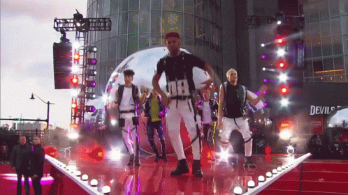 Men Dancing On Stage In Front Of Devil's Building GIF