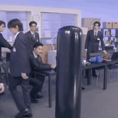 Men in Suits Standing Around Punching Bag