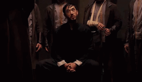 Men Standing Around Seated Man in Dark