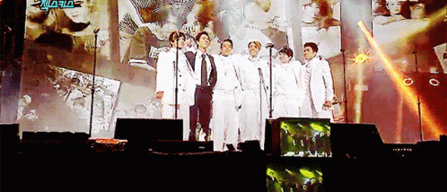 Men Standing on Stage With Microphones in Front of Screen Saying Aria