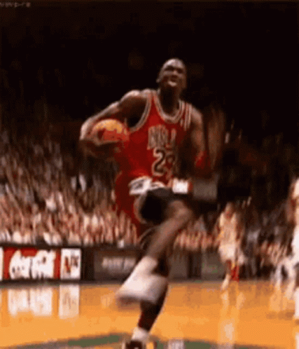 Michael Jordan Is Jumping In The Air While Holding A Basketball In His Hands . GIF