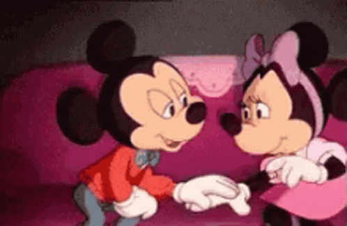 Mickey Mouse And Minnie Mouse Are Standing Next To Each Other On A Pink Couch Holding Hands . GIF