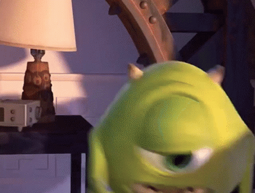 Mike Wazowski From Monsters Inc Is Standing In Front Of A Lamp On A Table GIF