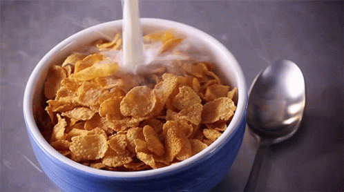 milk is being poured into a bowl of corn flakes