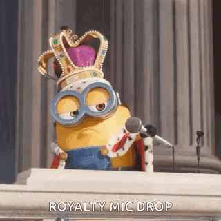 Minion Wearing Crown And Goggles Sitting At Podium Holding Microphone GIF