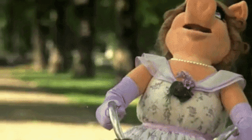 Miss Piggy From The Muppet Show Is Riding A Bike In The Park . GIF