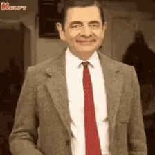Mr Bean Is Wearing A Suit And Tie And Smiling At The Camera . GIF