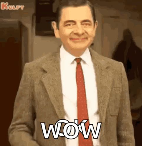 Mr Bean Is Wearing A Suit And Tie And Smiling With The Word Wow Written On His Chest . GIF