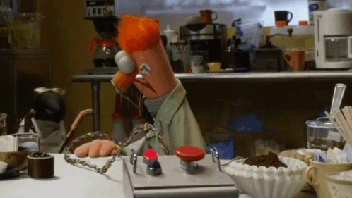 Muppet Sitting at Table With Red Button