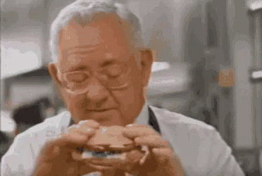 Older Man Eating Hamburger With Eyes Closed