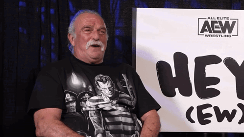 Older Man Sitting In Front Of Hey Crew Sign GIF