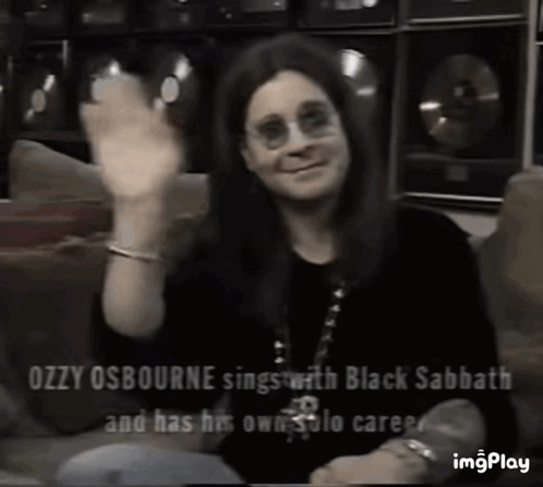Ozzy Osbourne Is Sitting On A Couch Waving His Hand . GIF