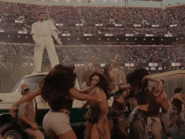 People Dancing in Stadium with Man in White Suit on Car