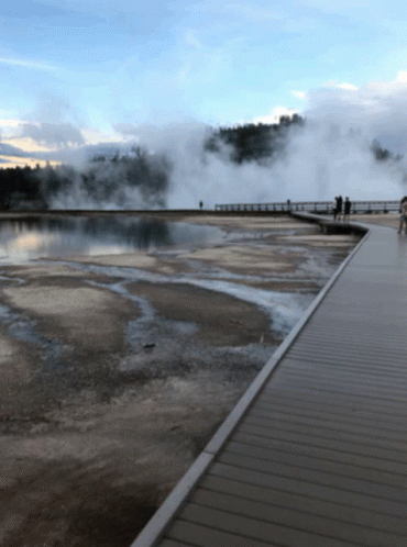 People Walking On A Boardwalk Overlooking A Body Of Water With Steam Coming Out Of It GIF