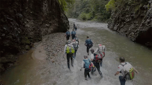 People Walking Through River With Backpacks GIF