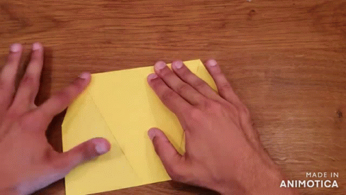 Person Folding Yellow Paper on Wooden Table