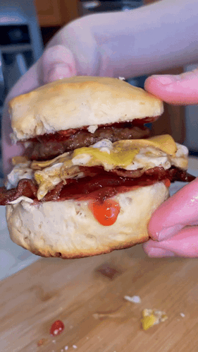 Person Holding Biscuit Sandwich With Eggs Bacon And Mustard GIF