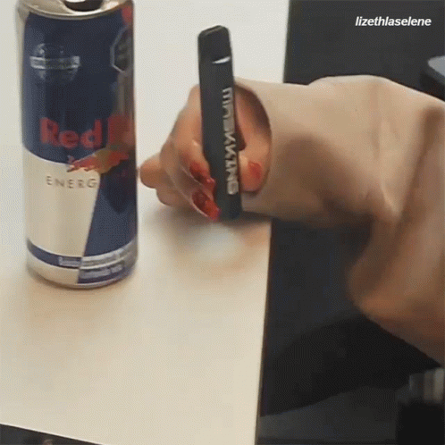 Person Holding Black King Device Next to Red Bull Can