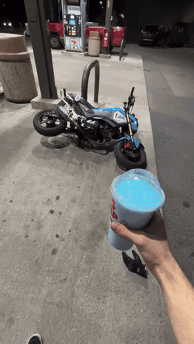 Person Holding Blue Drink in Front of Motorcycle