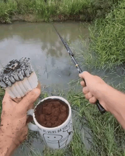 Person Holding Fishing Rod Next To Mug Saying As Vezes Da Vitoria GIF