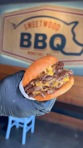 Person Holding Hamburger in Front of BBQ Sign