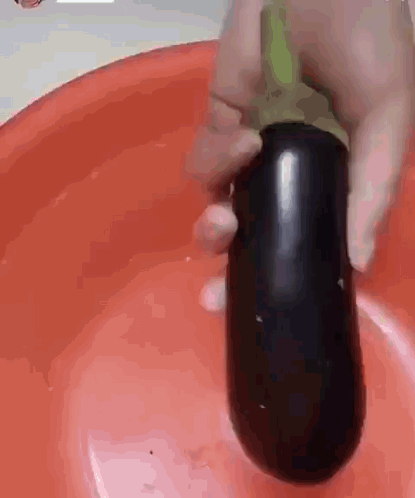 Person Holding Large Eggplant Over Red Bowl