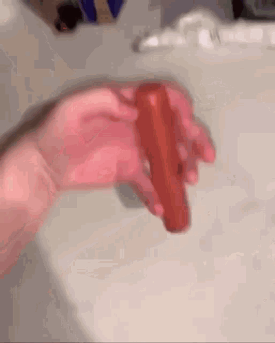 Person Holding Red Hot Dog in Front of Toilet