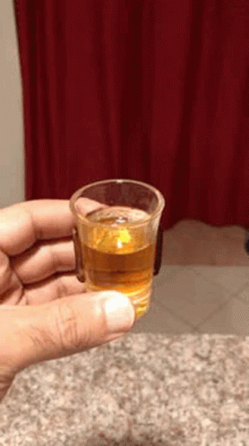Person Holding Shot Glass With Red Curtain Background