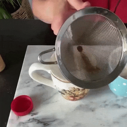 Person Holding Tea Strainer Over Cup