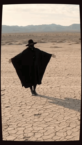 Person in Black Cape and Hat Arms Outstretched in Desert