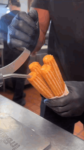 Person In Black Gloves Holding Churro In Front Of I-Ball Sign GIF