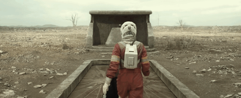 Person in Red Jumpsuit and White Helmet Walking Through Desert