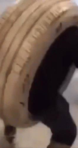 Person in White Jacket and Black Pants Carrying Large Tire